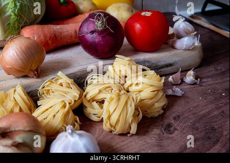 Asciugare la pasta italiana tagliatelle su un piano di lavoro della cucina insieme a varie verdure. Foto Stock