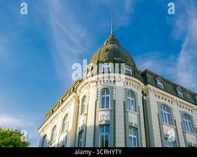 Elegante edificio storico con un tetto a cupola e finestre ad arco, catturate dalla calda luce del sole pomeridiano contro un cielo azzurro limpido, che mette in risalto la sua arcata Foto Stock