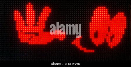 Primo piano di un luminoso display a LED rosso che raffigura un gesto giocoso della mano e un volto sorridente, scattato di notte su uno schermo digitale nero Foto Stock