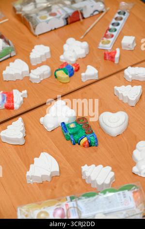 Un laboratorio per bambini sulla pittura di decorazioni natalizie su un tavolo di legno. Il nuovo anno è fatto a mano: Statuette in gesso bianco di alberi di Natale, cuori, e. Foto Stock