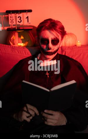 Uomo con il viso scheletro che legge un libro, in profondità, circondato dall'oscurità Foto Stock