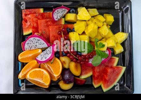 Piatto di frutta tropicale colorato con contorno alla menta. Assortimento luminoso e fresco di frutta tropicale a fette, tra cui anguria, drago, ananas Foto Stock