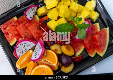 Vassoio di frutta fresca estiva con varietà tropicale. Vista dall'alto verso il basso di un piatto di frutta colorato con anguria, ananas, frutta del drago e arance Foto Stock