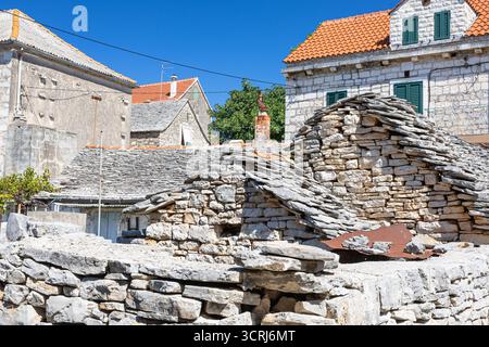 Un villaggio illuminato dal sole caratterizzato da case in pietra intemprata, muretti a secco sovrapposti e tetti di tegole rosse, che trasmettono fascino rustico e architettura tradizionale Foto Stock