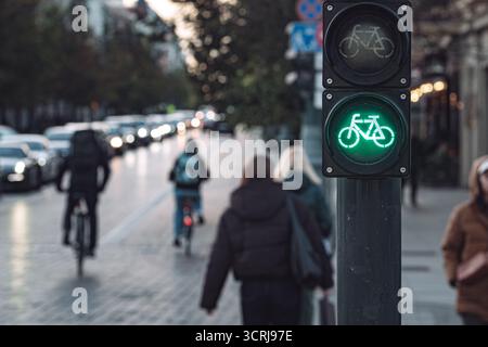 Primo piano del semaforo verde della bicicletta illuminato sulla trafficata strada della città con ciclisti e pedoni che pendono durante il giorno Foto Stock