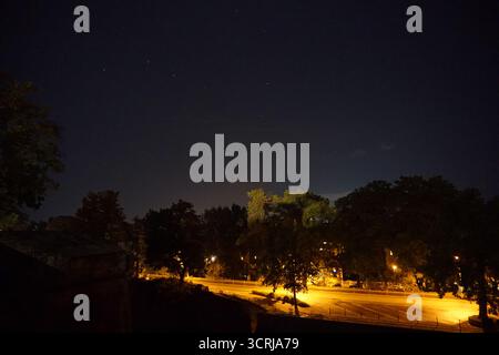 Il cielo notturno della città con vista sulla costellazione del "grande Orso" e su una strada illuminata con alberi che coprono l'orizzonte (Ursa maggiore) Foto Stock