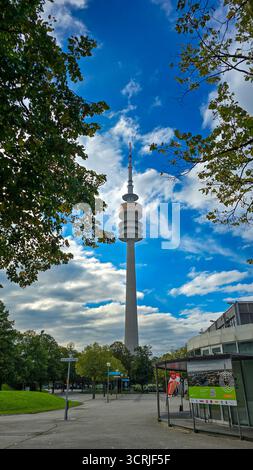 Vista della Torre Olimpica incorniciata da alberi verdi sullo sfondo del cielo blu. 27 settembre 2025. Monaco, Baviera, Germania. Foto Stock