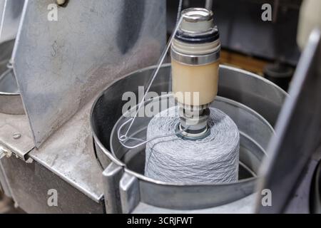 Il cono del filato scorre attraverso un alimentatore di tensione su una bobinatrice in una fabbrica tessile che mostra la preparazione per la lavorazione a maglia o la tessitura Foto Stock