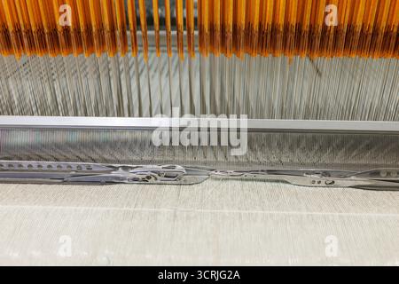 Vista ravvicinata della navetta presso la canna su un moderno telaio con ordito e trama in una fabbrica tessile che mostra tessitura di precisione e produzione di qualità Foto Stock