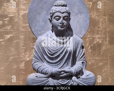 Primo piano di una statua di Buddha meditata su un trono di pietra di fronte a uno sfondo dorato Foto Stock