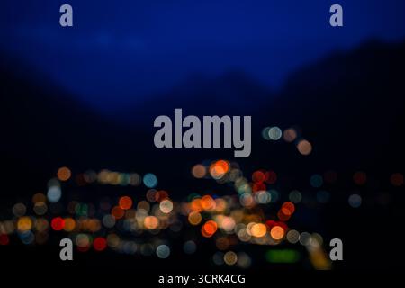 Le luci astratte della città brillano sotto una catena montuosa scura contro l'ora blu. Foto Stock