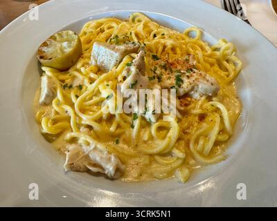 Un piatto di tagliatelle cremose condite con formaggio grattugiato ed erbe aromatiche, presentato su un tavolo rustico. Foto Stock