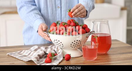 Donna con fragole fresche in colino e succo dolce in cucina, primo piano Foto Stock