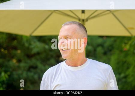 Un uomo felice sorride mentre si trova all'aperto sotto un grande ombrello. Foto Stock