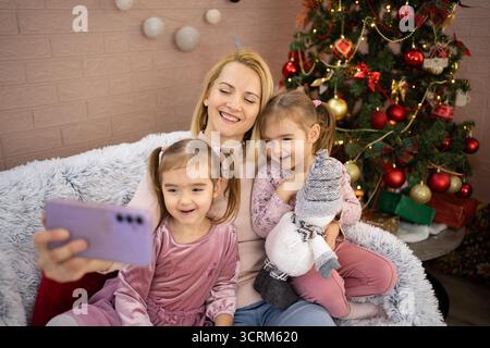 Madre e figlie si fanno selfie sull'albero di natale Foto Stock