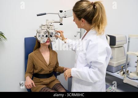 Optometrista che esegue l'esame oculare per il paziente che utilizza il phoropter Foto Stock