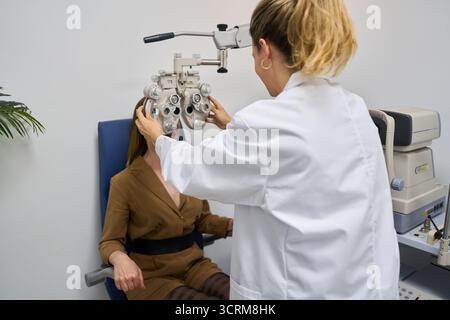 Optometrista che esegue un esame oculare utilizzando il phoropter per un paziente Foto Stock