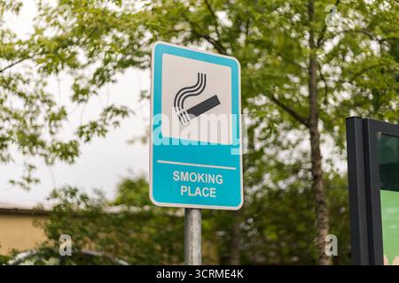 Un cartello che indica un'area fumatori designata è visibile in un parco verde. Gli alberi circostanti aggiungono un'atmosfera naturale al luogo per i fumatori Foto Stock