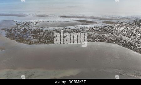 La vista aerea della tranquilla e scintillante zona intertidale rivela un arazzo di texture e colori, dove le distese sabbiose incontrano piscine poco profonde, Worthing, Inghilterra, Regno Unito. Foto Stock
