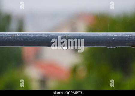 Goccioline d'acqua su una barra di ringhiera in metallo, ruggine che inizia a manifestarsi, sfondo sfocato per trasmettere un'atmosfera piovosa. Foto Stock