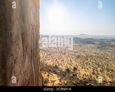 Liscia parete rocciosa di granito accanto a un'ampia vista panoramica della savana nebbiosa di Erongo e degli isolotti lontani da una cima rocciosa, la Namibia. Foto Stock