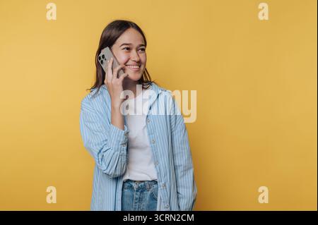 Giovane donna che parla con uno smartphone e sorride su uno sfondo giallo brillante Foto Stock