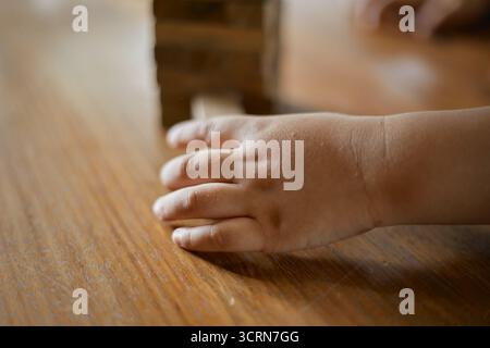 Primo piano tenendo la mano e giocando a Jenga o Tumble Tower Wooden Block Game Foto Stock