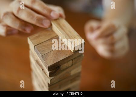 Primo piano tenendo la mano e giocando a Jenga o Tumble Tower Wooden Block Game Foto Stock