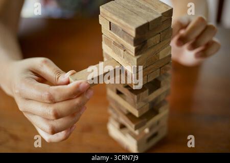 Primo piano tenendo la mano e giocando a Jenga o Tumble Tower Wooden Block Game Foto Stock