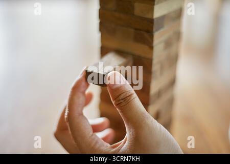 Primo piano tenendo la mano e giocando a Jenga o Tumble Tower Wooden Block Game Foto Stock