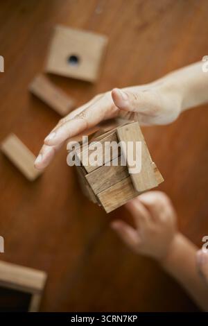 Primo piano tenendo la mano e giocando a Jenga o Tumble Tower Wooden Block Game Foto Stock