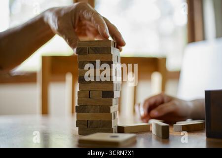 Primo piano tenendo la mano e giocando a Jenga o Tumble Tower Wooden Block Game Foto Stock