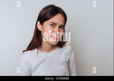 Una giovane donna con lunghi capelli marroni che indossa una camicia bianca, esprimendo scetticismo. Foto Stock