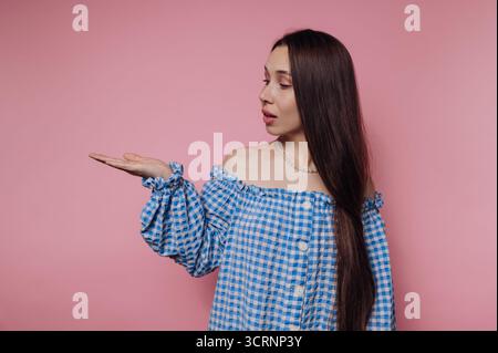 Una donna con un abito a scacchi a scacchi blu si muove con la mano su uno sfondo rosa. Foto Stock