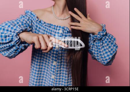 Una persona con capelli lunghi e lisci sta spazzolando i capelli delicatamente mentre è posizionata di fronte a una parete rosa. Foto Stock