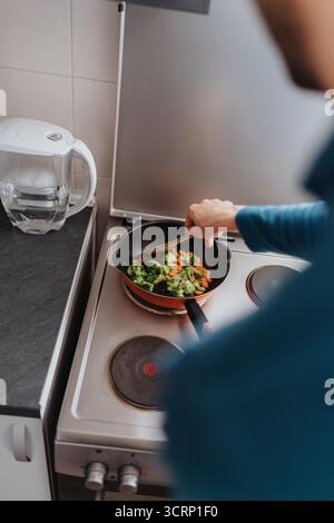 Persona che prepara una sana frittura di verdure su un piano cottura in una cucina di casa Foto Stock