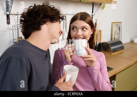 Una coppia gioiosa condivide un momento caldo nel loro moderno appartamento mentre si gusta un caffè insieme. Foto Stock