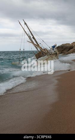Una barca bloccata ora poggia su una spiaggia sabbiosa, con onde che si infrangono continuamente sotto un cielo grigio e nuvoloso Foto Stock