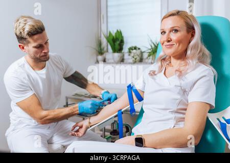 Un operatore sanitario sta prelevando sangue da un paziente sorridente in un ambiente medico pulito. Foto Stock