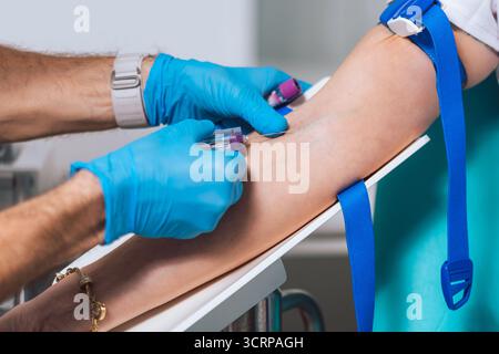 L'assistente di laboratorio inserisce un ago nella vena su un braccio del paziente con un laccio emostatico posizionato e preleva il sangue con una provetta Vacutainer. Foto Stock