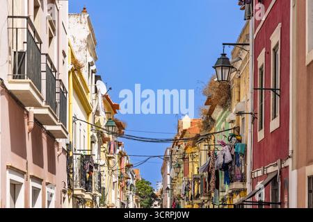 Una strada stretta e' incorniciata da alti e tradizionali edifici con facciate e balconi dai colori vivaci dove e' appesa la lavanderia, il tutto sotto un blu luminoso Foto Stock