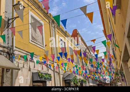 Le vivaci bandiere triangolari in più colori sono appese su una strada soleggiata con facciata gialla a Setubal, Portogallo, creando un'atmosfera festosa Foto Stock