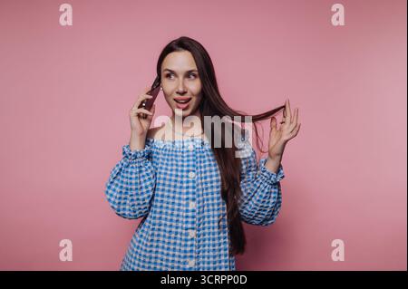 Donna in abito a scacchi blu che parla al telefono su sfondo rosa. Foto Stock