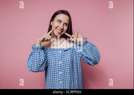 Giovane donna in abito a scacchi blu che posa giocosamente su sfondo rosa. Foto Stock