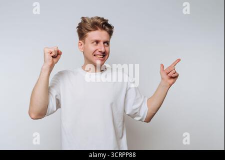 Giovane uomo con t-shirt bianca che punta e sorride su sfondo bianco. Foto Stock