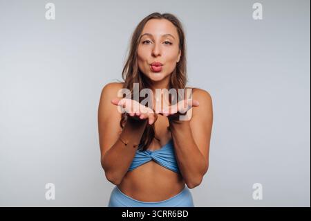 Una donna che indossa un abito azzurro si trova in uno studio, e fa un bacio giocoso. Ha lunghi capelli castani e un sorriso brillante, che si aggiunge alla allegra a a Foto Stock