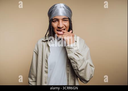 Un giovane sorride e morde giocosamente il dito indossando un copricapo argentato. Lo sfondo è semplice e di colore chiaro, per creare un divertimento e un'atmosfera casu Foto Stock