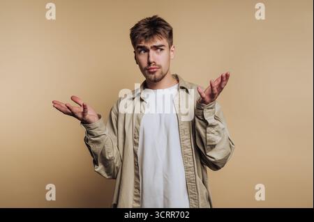 Un giovane uomo si trova in uno studio, vestito con un outfit casual, con un'espressione neutra. Gestiva con le mani, apparendo sconcertato o incerto abou Foto Stock