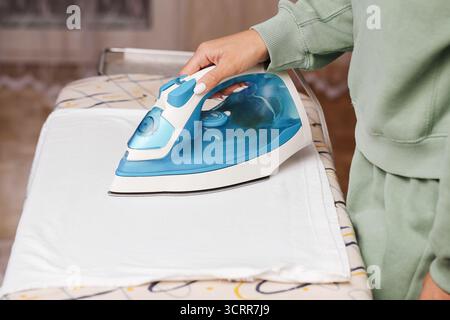 Donna che stirava vestiti a bordo. Lavoro domestico e compito domestico. Pulizia del tessuto e del ferro da stiro. Dettagli della routine domestica e dei lavori domestici. Foto Stock