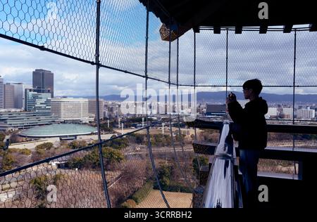 I visitatori catturano la città dalla piattaforma di osservazione superiore del castello di Osaka in inverno Foto Stock